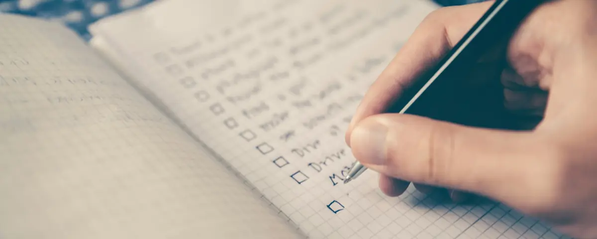 A hand ticking off a to-do list in a squared notebook