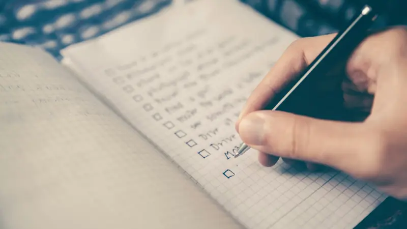 A hand ticking off a to-do list in a squared notebook
