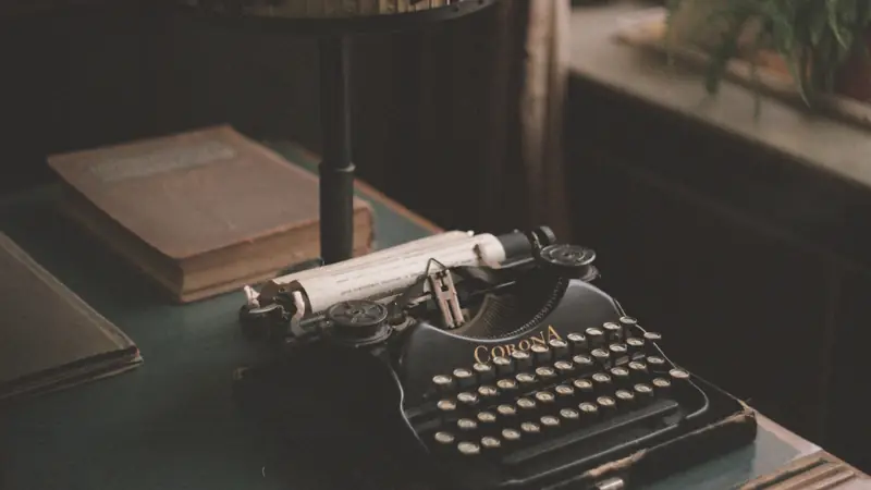 A vintage typewriter with a sheet of paper in it, next to an old book