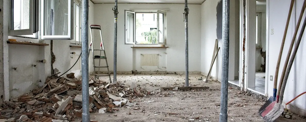 A room under renovation, its ceiling held up by metal props, rubble on the floor