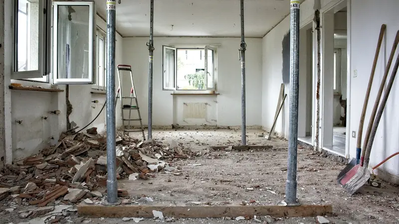 A room under renovation, its ceiling held up by metal props, rubble on the floor