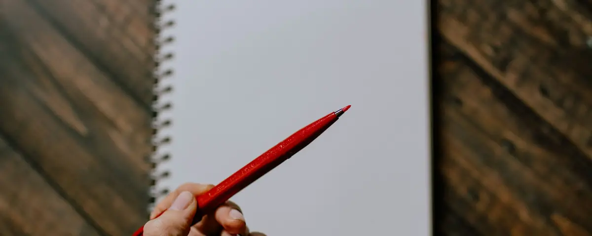 A hand holding a red pen over a notebook