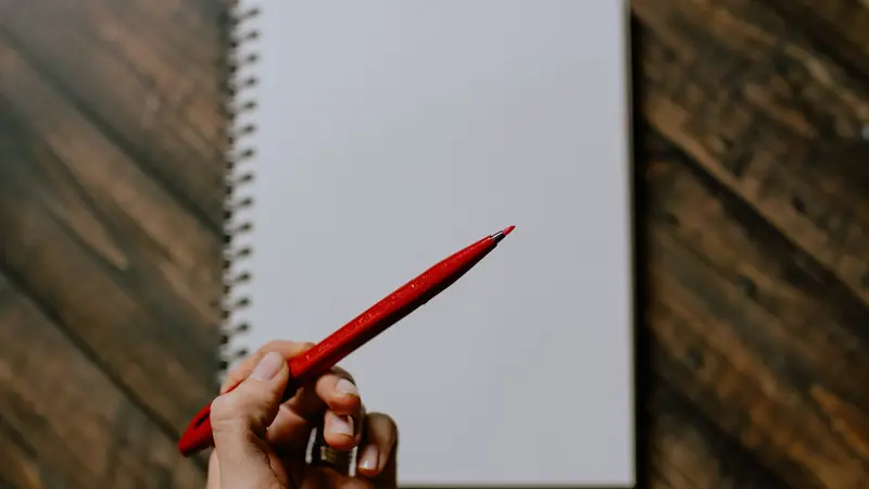 A hand holding a red pen over a notebook