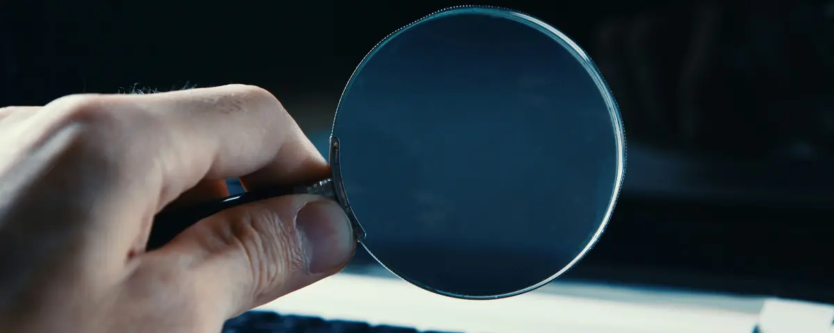 A hand holding a magnifying glass in front of a computer screen